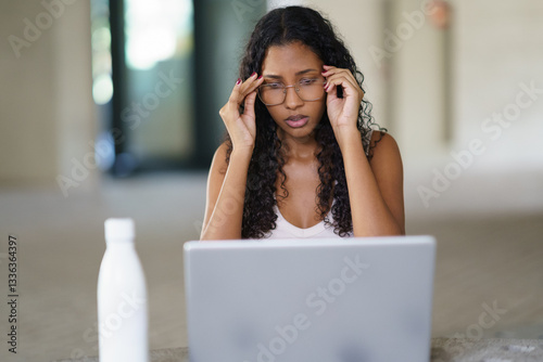 A stressed woman is diligently working on her laptop in a modern and stylish workspace