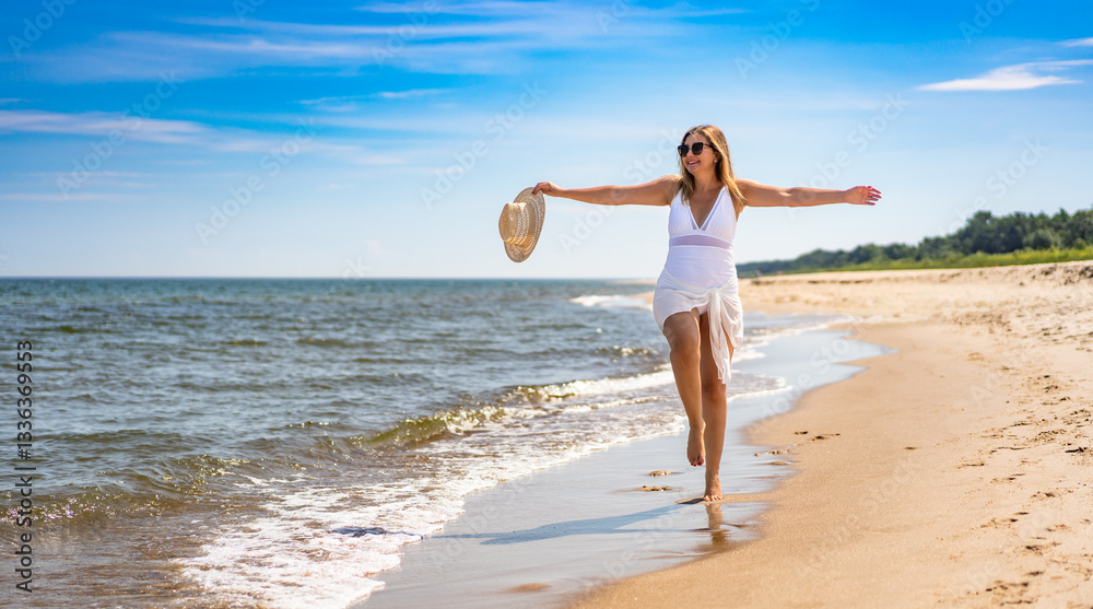 Beautiful middle-aged woman in swimsuit walking with outstretched arms on sandy beach in summertime. Energy and happiness. Front view Beautiful middle-aged woman in swimsuit walking with outstretched arms on sandy beach in summertime. Energy and happiness. Front view