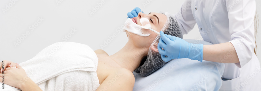 Fototapeta premium Young woman enjoying a luxurious professional facial mask treatment, enhancing her skin's radiance. A day at the spa, beauty treatment, and relaxing skincare session.