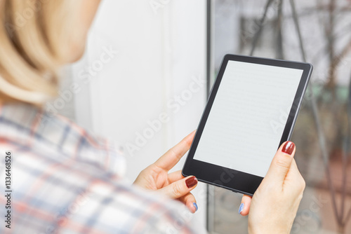 Wallpaper Mural woman reading e-book standing near window in house. girl reading e-book at home. female hand holding an e-book. ebook mockup. place for inscription.  Torontodigital.ca