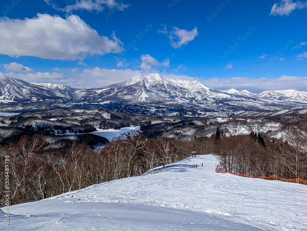 Narrow ski slope with snow covered jagged mountains and trees. Madarao, Japan