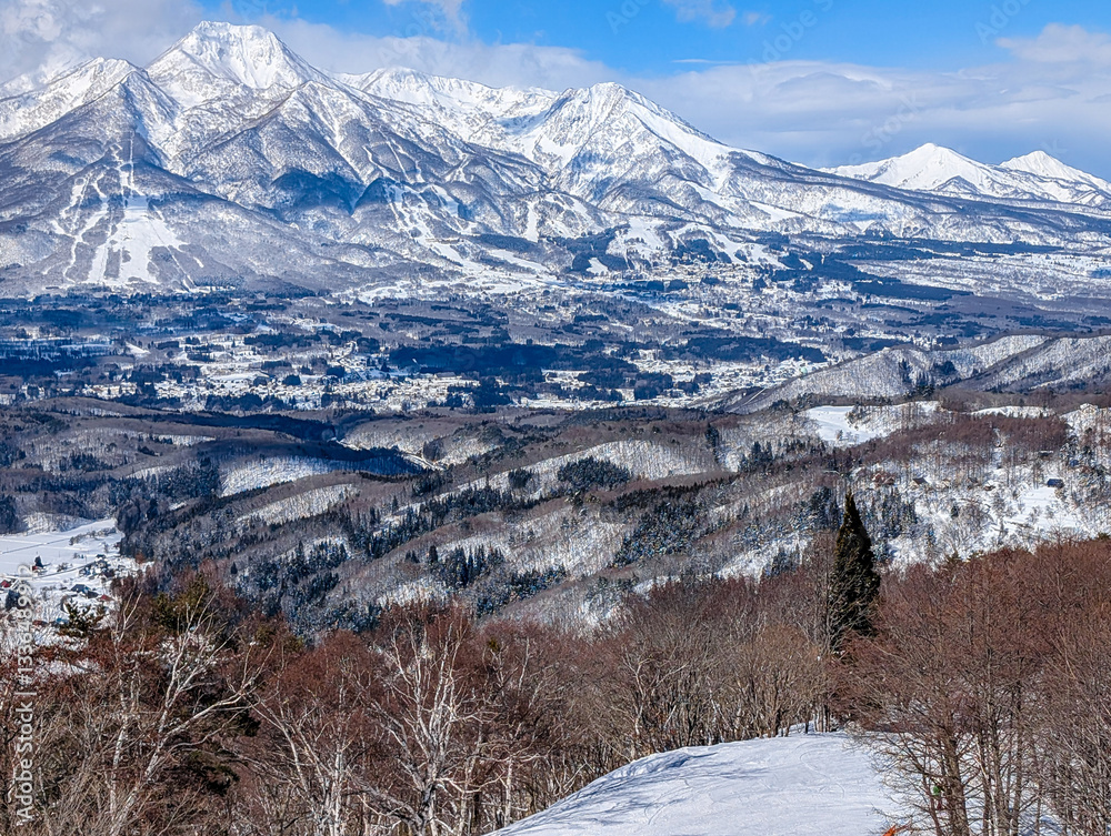 Narrow ski slope with snow covered jagged mountains and trees. Madarao, Japan