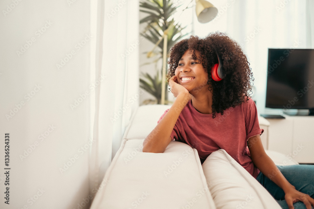 Happy African American woman relaxing on the sofa at home. Smiling girl enjoying holiday sitting on couch, listen music and looking outside. Healthy lifestyle, good vibes people and new home concept.. Happy African American woman relaxing on the sofa at home. Smiling girl enjoying holiday sitting on couch, listen music and looking outside. Healthy lifestyle, good vibes people and new home concept..