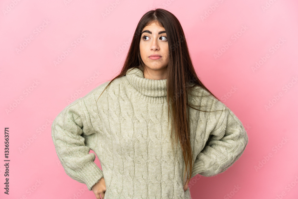 Fototapeta premium Young caucasian woman isolated on pink background making doubts gesture looking side