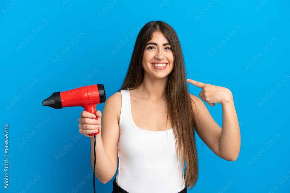 Young caucasian woman holding a hairdryer isolated on blue background giving a thumbs up gesture Young caucasian woman holding a hairdryer isolated on blue background giving a thumbs up gesture