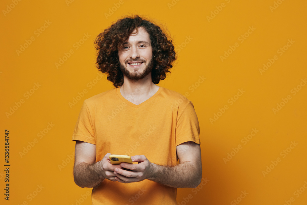 Smiling young man using smartphone, wearing a vibrant orange t shirt against a bright orange background, embodying a joyful and modern lifestyle Smiling young man using smartphone, wearing a vibrant orange t shirt against a bright orange background, embodying a joyful and modern lifestyle