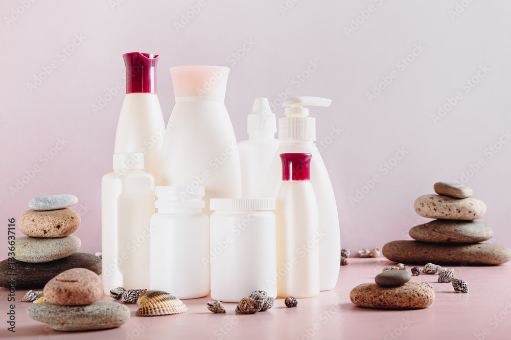 Set of bottles with cosmetic products among stones and shells on pink