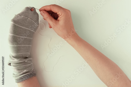 Caucasian woman sewing a hole in her sock with a needle and thread. White background.