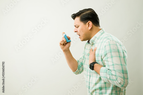 Hispanic man having respiratory problems and using blue asthma inhaler during asthma attack photo