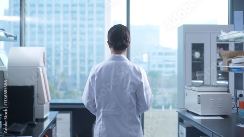 Photos Female researcher standing with back to camera in laboratory surrounded by scien