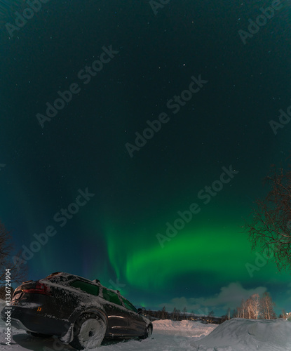 Fotografi Green aurora borealis illuminating the night sky above a snow covered landscape