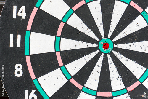 Detailed view of a well-used dartboard with colorful segments and a vibrant bullseye in a casual setting