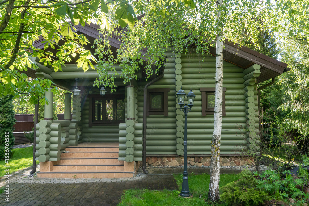 A wonderful wooden house made of logs surrounded by green trees, the foliage of which is illuminated by sunlight. A wonderful wooden house made of logs surrounded by green trees, the foliage of which is illuminated by sunlight.