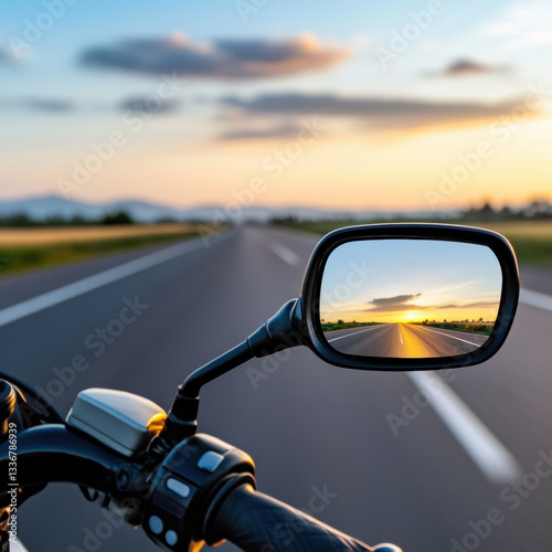 motorcycle rearview mirror reflects scenic road at sunset, evoking sense of adventure and freedom