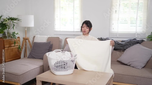 Asian woman folding laundry while relaxing on the couch in a cozy living room
