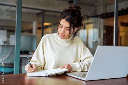 Quadro su tela Young latina or indian business woman using laptop pc working at desk writing notes, watching educational online webinar
