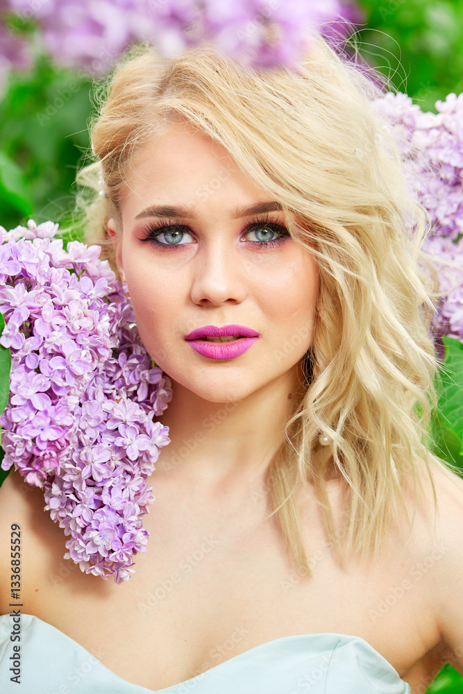 Blonde with blue eyes and pink lipstick stands with purple flowers. She is wearing pearl earrings and a pink dress. The image has a soft and romantic mood, with the beauty of the woman. Close-up portr Blonde with blue eyes and pink lipstick stands with purple flowers. She is wearing pearl earrings and a pink dress. The image has a soft and romantic mood, with the beauty of the woman. Close-up portr
