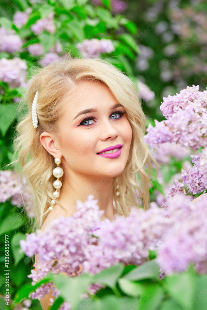 Blonde with blue eyes and pink lipstick stands with purple flowers. She is wearing pearl earrings and a pink dress. The image has a soft and romantic mood, with the beauty of the woman. Close-up portr Blonde with blue eyes and pink lipstick stands with purple flowers. She is wearing pearl earrings and a pink dress. The image has a soft and romantic mood, with the beauty of the woman. Close-up portr