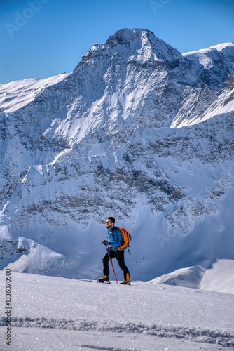 A young man on a ski tour in the Swiss Alps. Fantastic winter sports weather in the mountains of Glarus, Switzerland. Ski mountaineering surrounded by tall mountains. Skitour above Elm. Hausstock.
