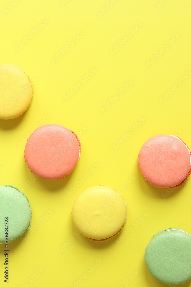 Bright French macarons on yellow background, top view. Assortment of multi-colored macarons with different flavors. Delicious pastries, flat lay. Food background. Sweets