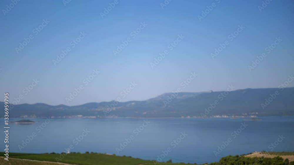 Dreamy blurred seascape with a small island in the center. Mountains on the horizon and vineyards in the foreground, creating a soft and romantic ambiance. Ideal for travel videos. Dreamy blurred seascape with a small island in the center. Mountains on the horizon and vineyards in the foreground, creating a soft and romantic ambiance. Ideal for travel videos.