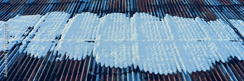 snow on rusty corrugated iron sheets of a barn roof
