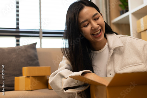 A woman is holding two boxes and smiling. She is sitting in front of a laptop. The boxes are brown and appear to be gifts. The woman seems happy and excited about the boxes
