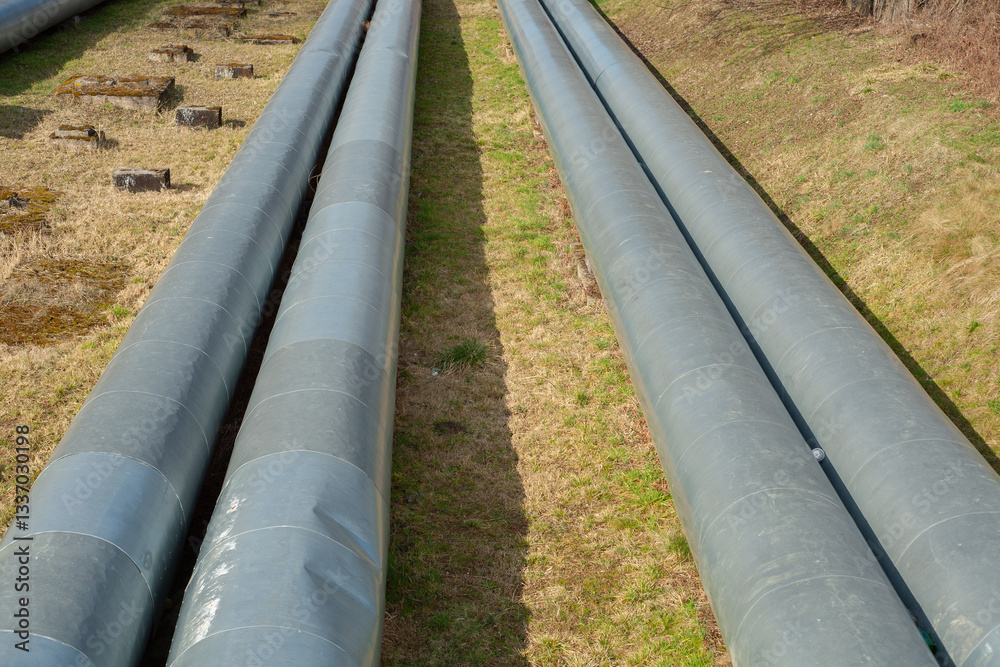 Top view of large above-ground pipelines running across a grassy strip. Part of an industrial energy or heating network used for fluid or gas distribution Top view of large above-ground pipelines running across a grassy strip. Part of an industrial energy or heating network used for fluid or gas distribution
