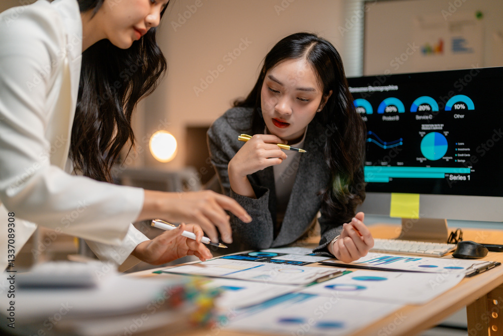 Fototapeta premium Businesswomen analyzing financial charts and graphs, working late in office