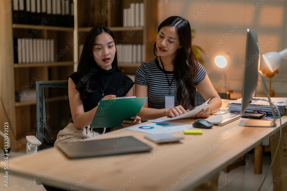 Two businesswomen are discussing work using laptop and financial documents at the office Two businesswomen are discussing work using laptop and financial documents at the office
