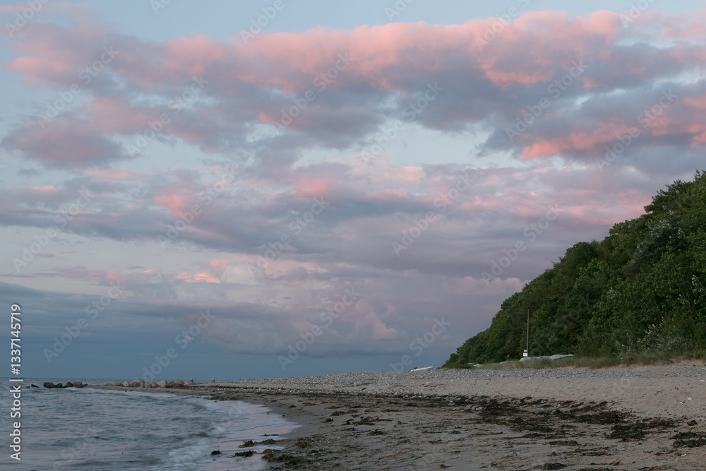 Ostseestrand mit Steilküste und Wald nach Sonnenuntergang.