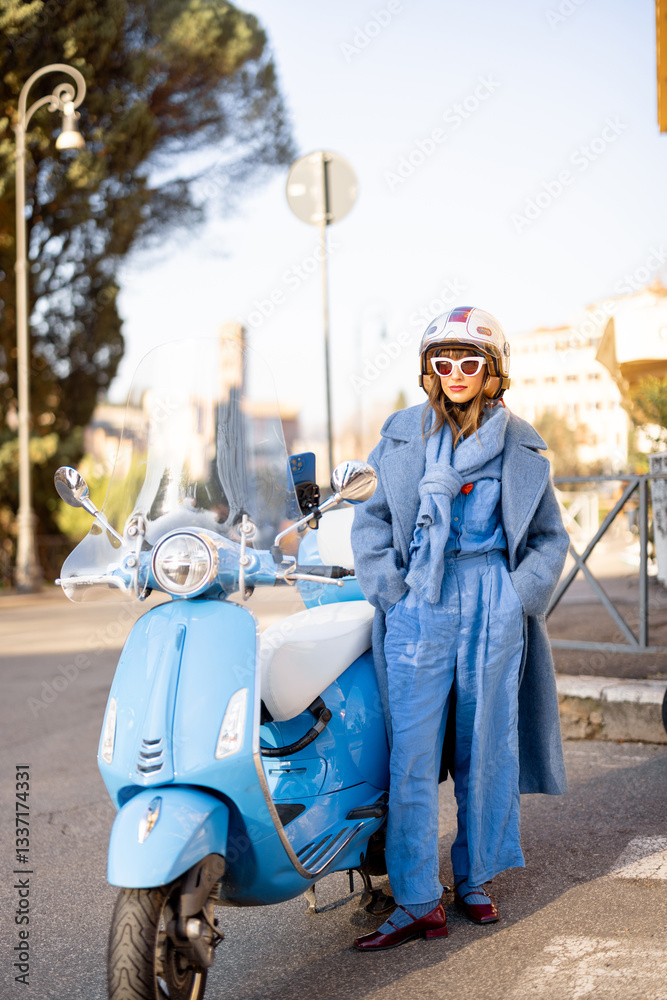 A stylish woman in a blue jumpsuit and coat stands confidently next to her scooter on a sunny day in Rome, Italy. A perfect representation of Italian elegance, city lifestyle, and independent travel