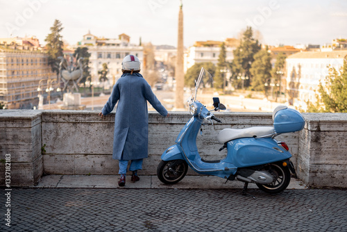 Obraz na płótnie A stylish woman in a long blue coat and helmet stands, overlooking the historic cityscape of Rome with an obelisk in the background. Scooter parked nearby adds to the charm of Italian exploration w salonie