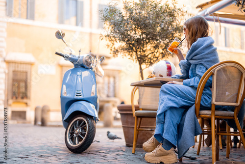 Obraz na płótnie A fashionable Italian woman sits at a cozy outdoor cafe in Rome, sipping an aperitivo. Her scooter is parked nearby, adding to the effortless elegance of Italian city life w salonie