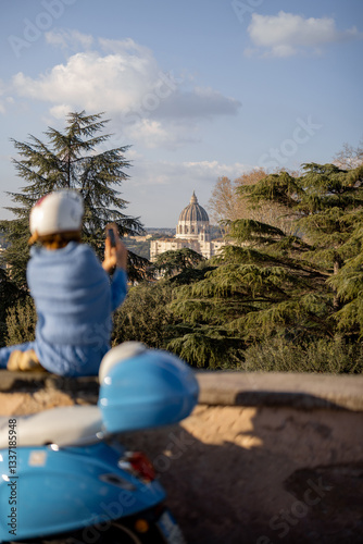 Obraz na płótnie A traveler captures a scenic view of St. Peters Basilica in Vatican City from a high vantage point in Rome. A classic blue scooter in the foreground adds to the charm of Italian exploration w salonie
