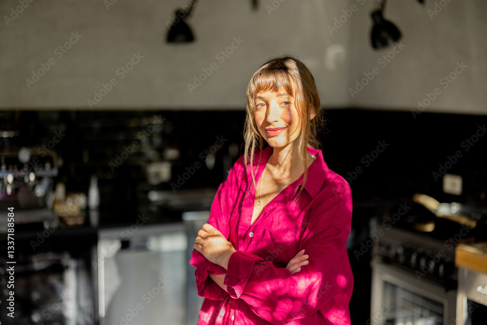A woman in a pink oversized shirt stands in a modern kitchen, illuminated by natural sunlight. The scene evokes warmth, mindfulness, and a relaxed morning routine in a contemporary home