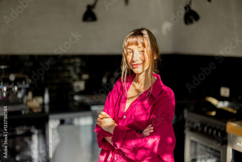 Obraz na płótnie A woman in a pink oversized shirt stands in a modern kitchen, illuminated by natural sunlight. The scene evokes warmth, mindfulness, and a relaxed morning routine in a contemporary home w salonie