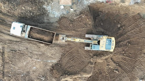 A large construction vehicle is pulling a trailer with a large bucket on the back. The bucket is filled with dirt and rocks. The scene is a construction site, and the vehicle is likely a bulldozer
