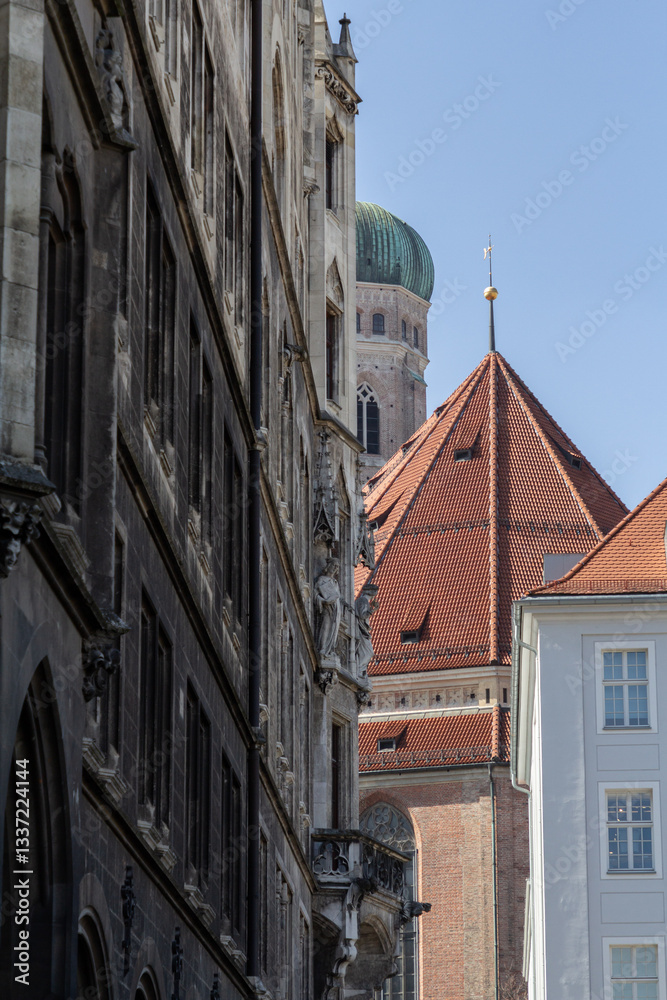Naklejka premium The tower of Frauenkirche in Munich, Germany, seen through surrounding buildings, offering a unique view of the city's architecture.