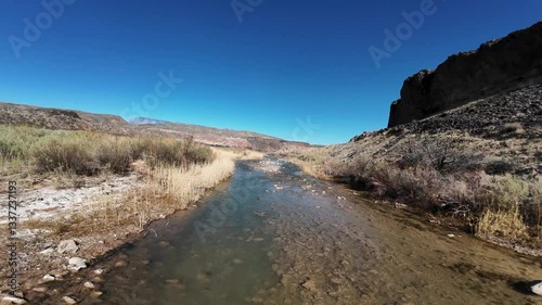 Virgin River Gorge- Hurricane, Utah, USA - February 10, 2025: Aerial-FPV-Chasing drone shadow over seasonally shallow rocky river under clear blue sky 