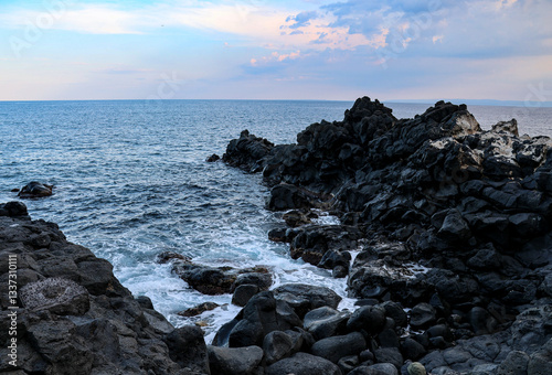 Black lava rock outcropping juts out into the Ionian Sea at Aci Castello, Catania, Sicily at sunset