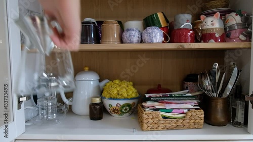 Coffee Brewing in a Stylish Kitchen – Hand Selecting Glass Coffee Maker with Colorful Tea Cups in Cabinet