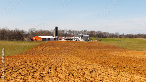 A large farm in Middle Tennessee features red outbuildings in the background, while freshly plowed fields of rich red soil stretch across the foreground, marking the start of early spring planting.