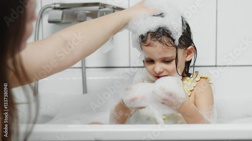 little girl bathes and washes her hair in soap suds.