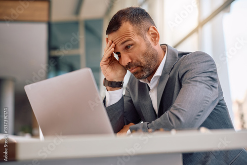 Worried businessman reading problematic email on computer at corporate office.
