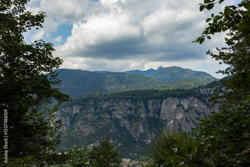 catena montuosa lontana nelle Alpi del nord Italia, vista da dietro le sagome degli alberi di un bosco, di giorno, in estate