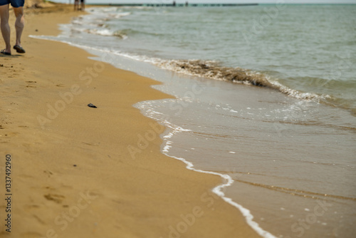 vista dettagliata sul bagnasciuga di una spiaggia, di giorno, in estate, bagnato dall'acqua del mare Adriatico, con le gambe di una persona che cammina sullo sfondo