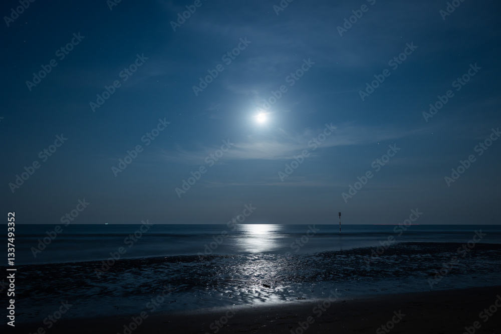 panoramica notturna su un ambiente marino sul mare Adriatico dalla costa della regione Veneto, con mare calmo, mentre la luna si riflette sull'acqua, in estate