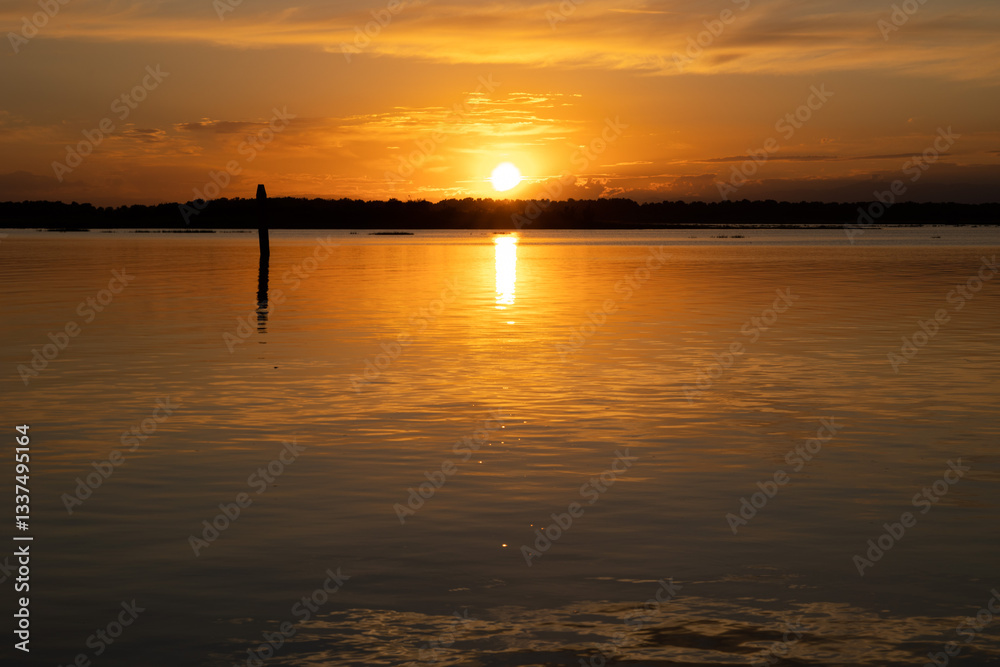 tramonto su una laguna in un ambiente marino tranquillo, nella regione Veneto, con cielo sereno, in estate, che si riflette sull'acqua