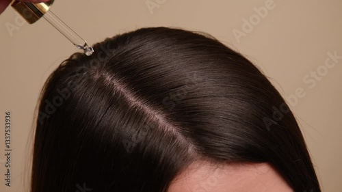 Beautiful woman with brown healthy hair applying oil or serum to roots on beige background. Hair beauty